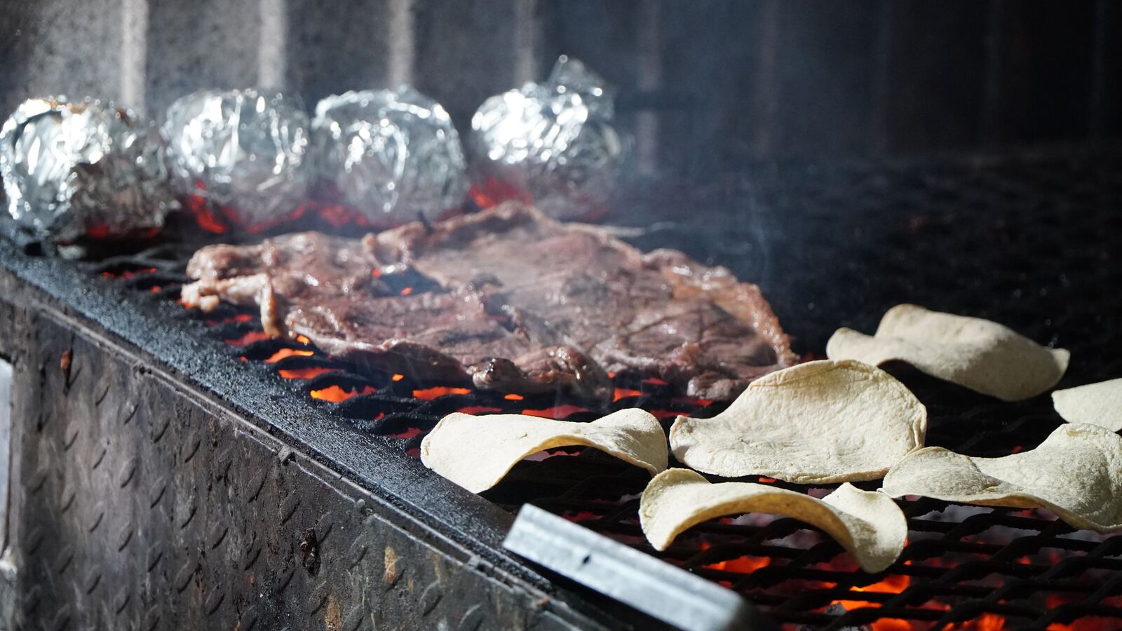 Carne asándose sobre el carbón con tortillas y chiles