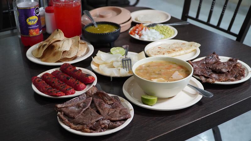 Mesa servida con carne, salchichas, charros, guacamole y tortillas